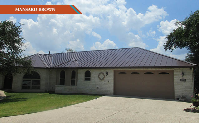 A Mansard Brown style metal roof on a white rock one story house with a driveway in front.